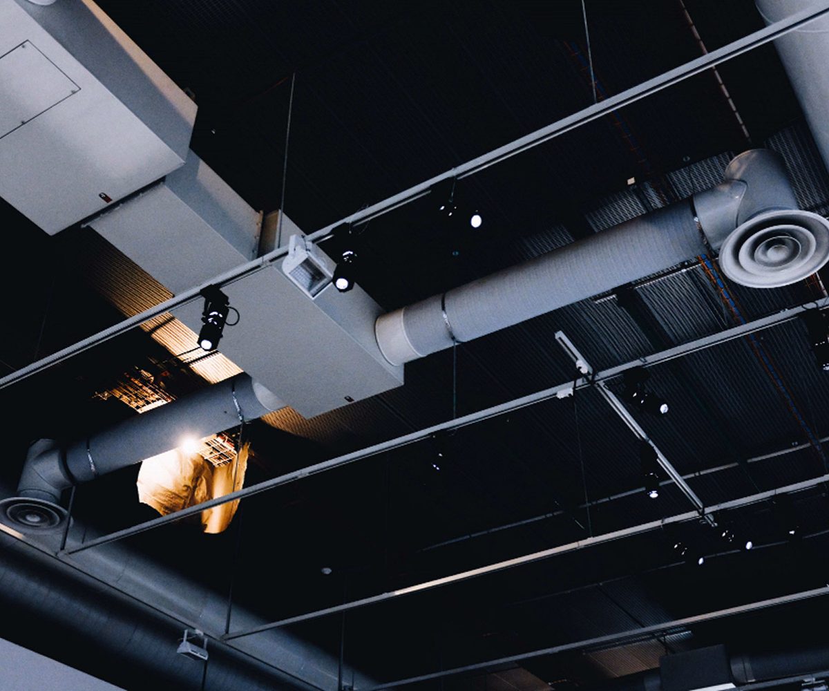 Technician working above a suspended ceiling near ventilation ducts